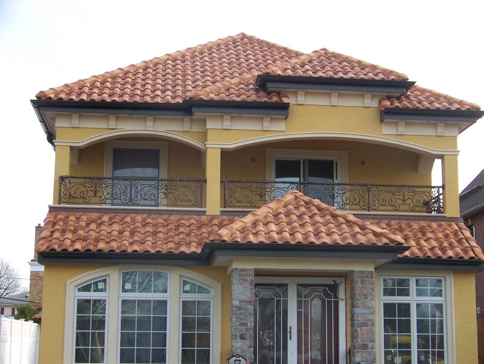 Golden-stucco home with balcony and terracotta clay tile roof