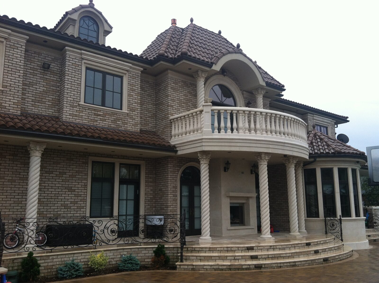 Grand grey-brick home with curved colonnade balcony and clay tile roof