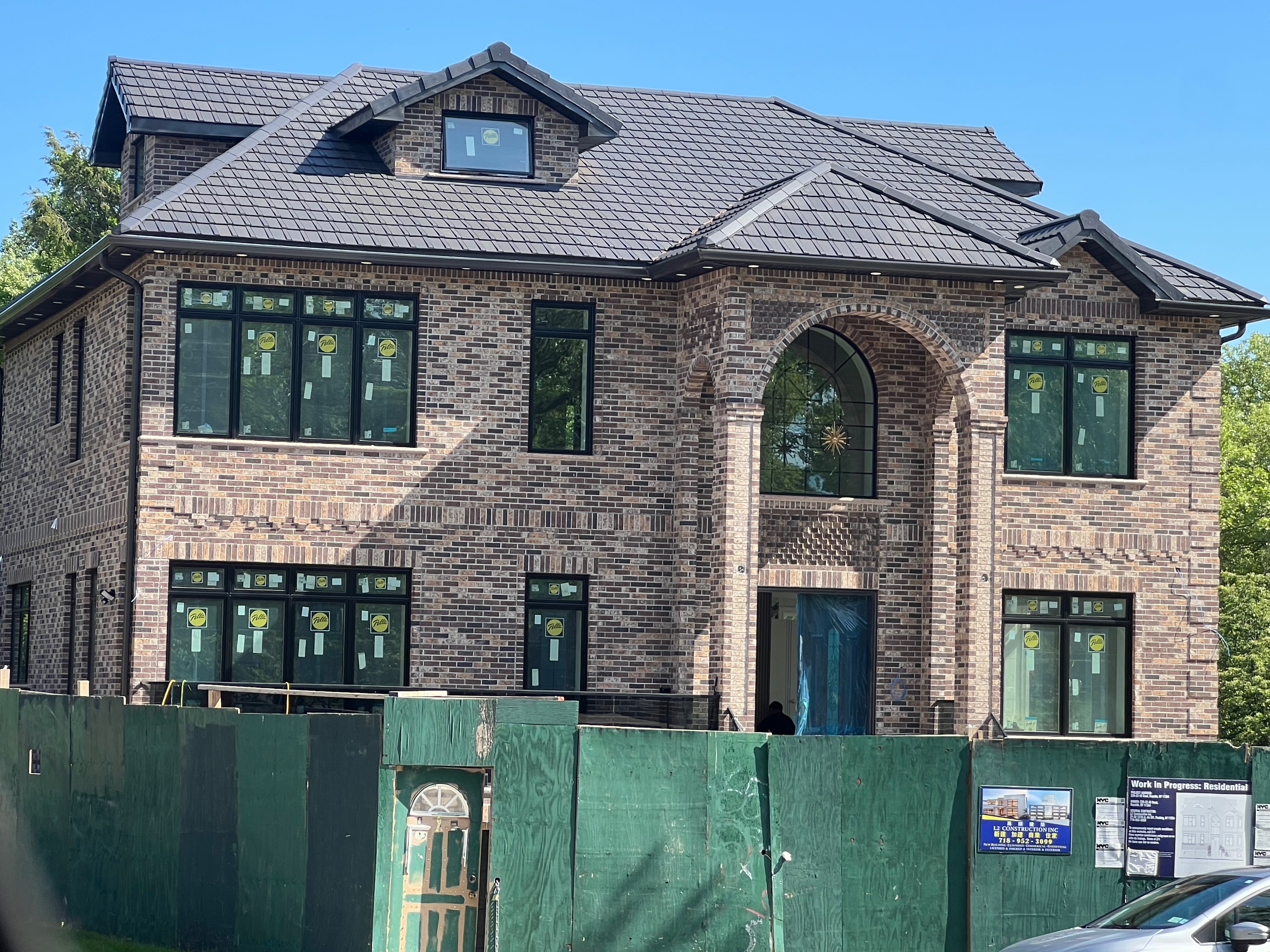 Large brick home under construction with sophisticated gray charcoal clay tile roofing